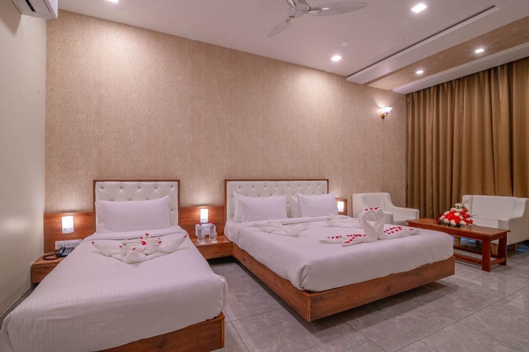 Une chambre d’hôtel avec deux lits, un ventilateur de plafond, une table de chevet en bois avec un téléphone et une petite table sur laquelle est posé un vase de fleurs.