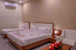 Una camera d'albergo con due letti, un comodino in legno, una poltrona bianca e un vaso di fiori.