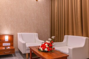 Una stanza con due divani bianchi, un tavolo di legno con un'esposizione floreale, un comodino con una lampada e una finestra con tende.