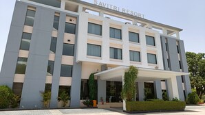 Ein modernes Gebäude mit dem Schild "SAVITRI RESORT" oben. Es zeigt eine mehrstöckige Struktur mit großen Fenstern und einem überdachten Eingangsbereich.