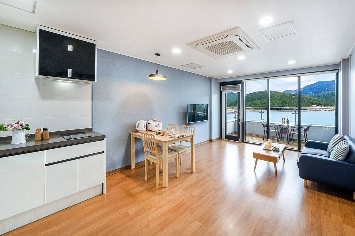 A modern kitchen with a dining area, a sofa, and a balcony with a scenic view.