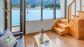 A modern living room with large windows, a wooden staircase, and a view of a lake and mountains.