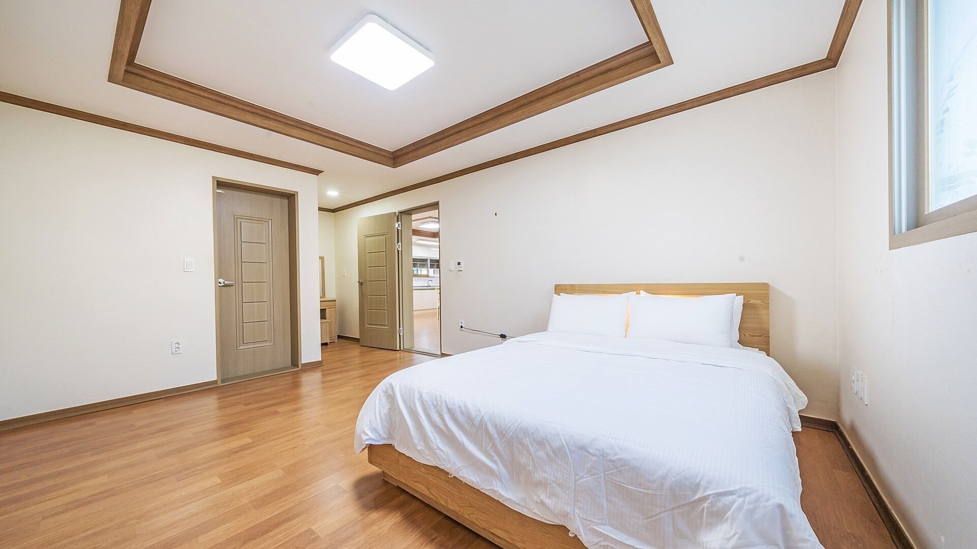 Une chambre avec un lit en bois, une lucarne et un couloir menant à une salle de bain.