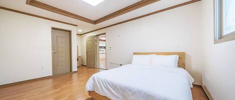 Une chambre avec un lit en bois, une lucarne et un couloir menant à une salle de bain.