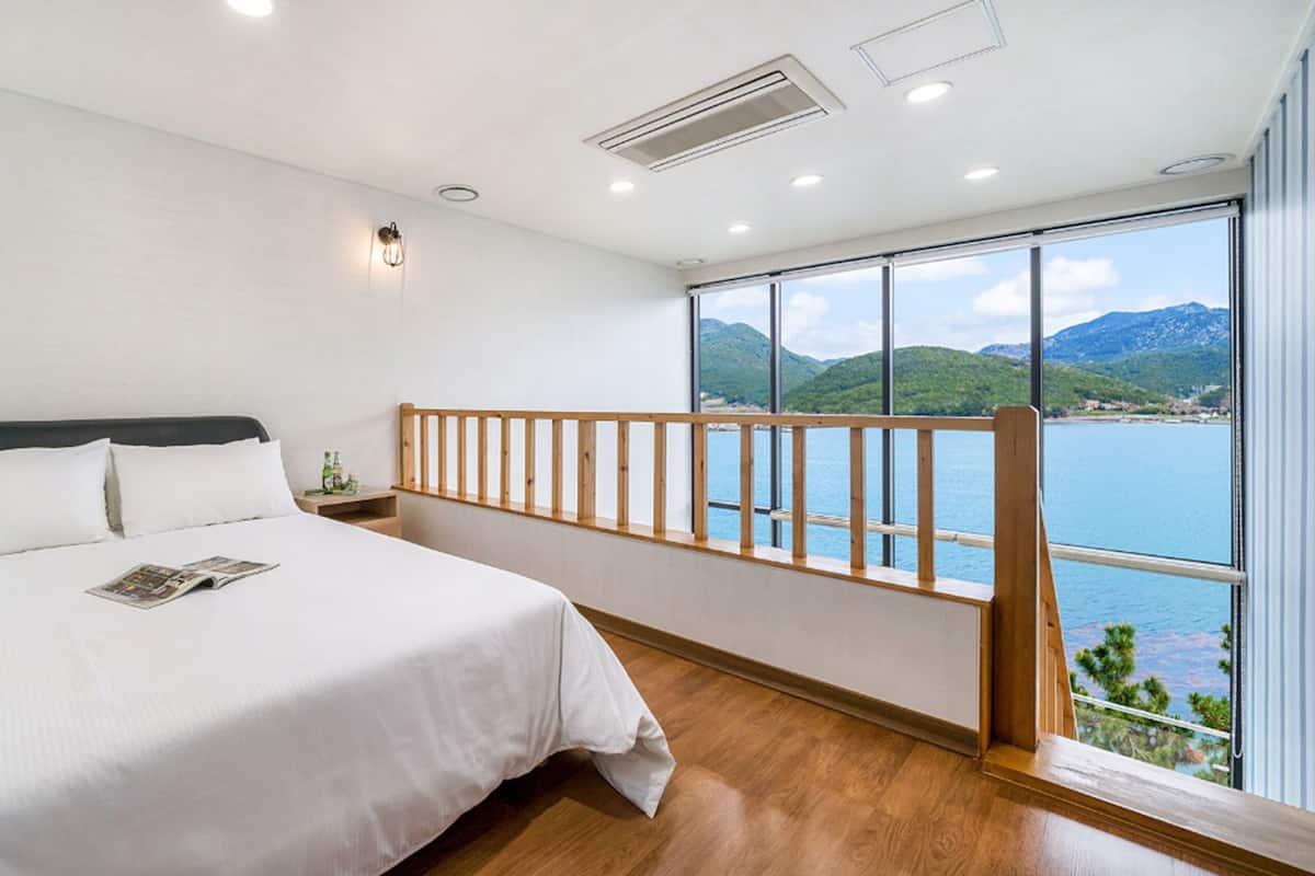 A bedroom with a bed, a nightstand, a wooden railing, and a large window with a mountain view.