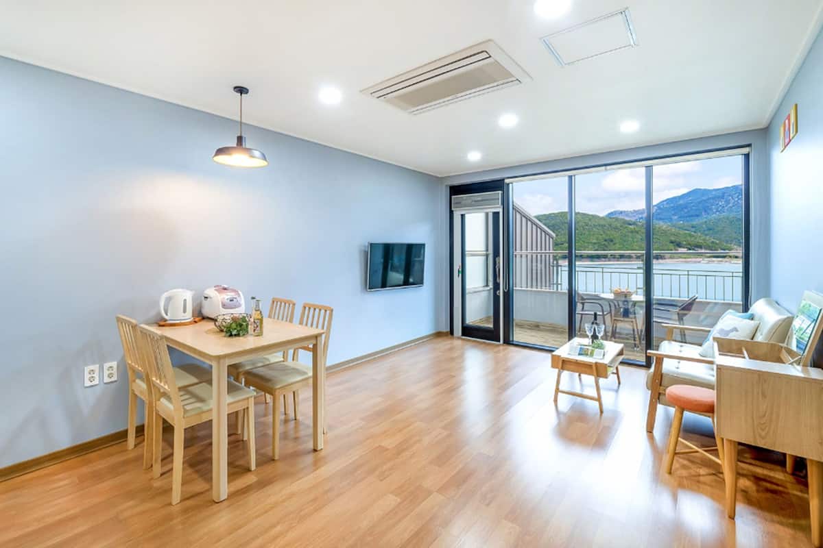 A spacious room with a wooden dining table, chairs, a sofa, and a TV mounted on the wall.