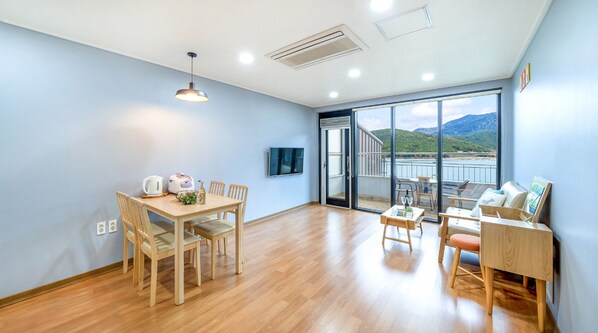 A spacious room with a wooden dining table, chairs, a sofa, and a TV mounted on the wall.