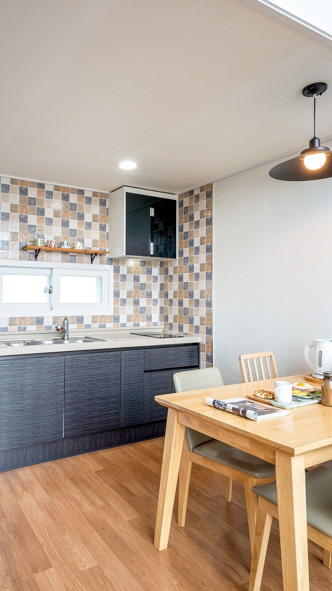 A modern kitchen with a tiled backsplash, a built-in oven, and a dining area with a wooden table and chairs.
