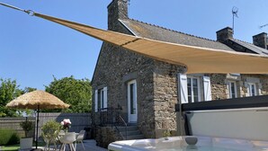 Uma casa de pedra com hidromassagem, um deck de madeira e um guarda-sol de palha.