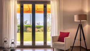 Une pièce dotée d’une porte-fenêtre coulissante donnant sur un jardin, d’un fauteuil blanc avec un coussin rouge et d’un lampadaire.