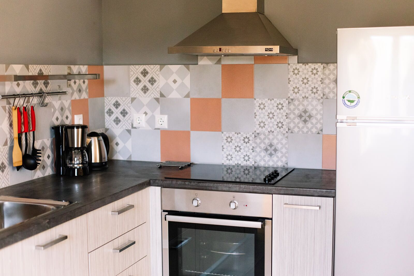A modern kitchen with a stainless steel range hood, a built-in oven, and a white refrigerator.