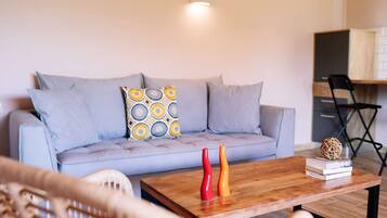 A living room with a light blue sofa, patterned pillows, a wooden coffee table, and a small bookshelf.