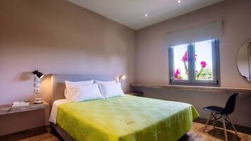 A bedroom with a bed, bedside table, lamp, chair, and a window with flowers.