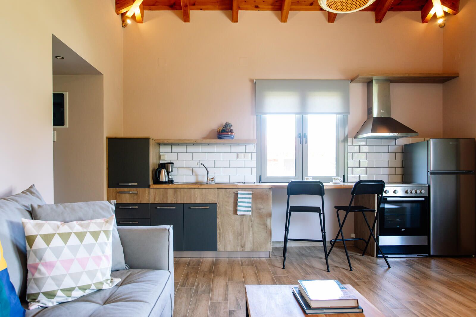 A modern kitchen with a central island, a dining area with two chairs, a sofa with cushions, and a refrigerator.