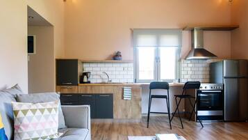 A modern kitchen with a central island, a dining area with two chairs, a sofa with cushions, and a refrigerator.