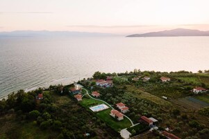 Vista aérea de una zona residencial costera con casas, una piscina y vistas al mar y montañas distantes.