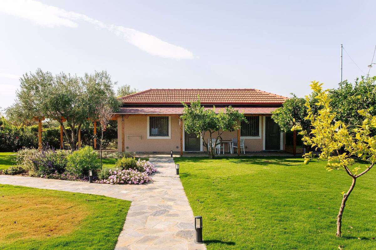 A house with a red-tiled roof, a stone pathway leading to the entrance, and a well-maintained garden with various plants and a small tree.