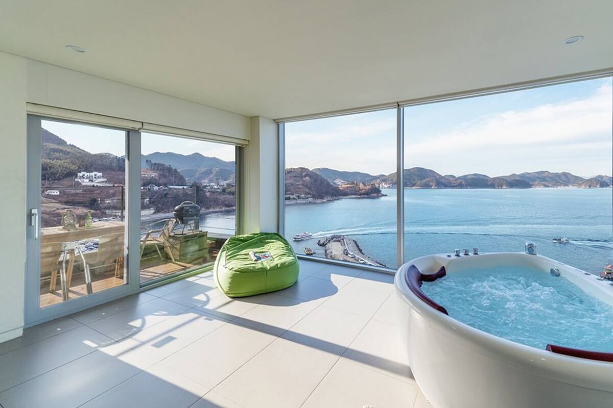 A spacious room with a large sliding glass door leading to a balcony, a jacuzzi, and a green bean bag chair.