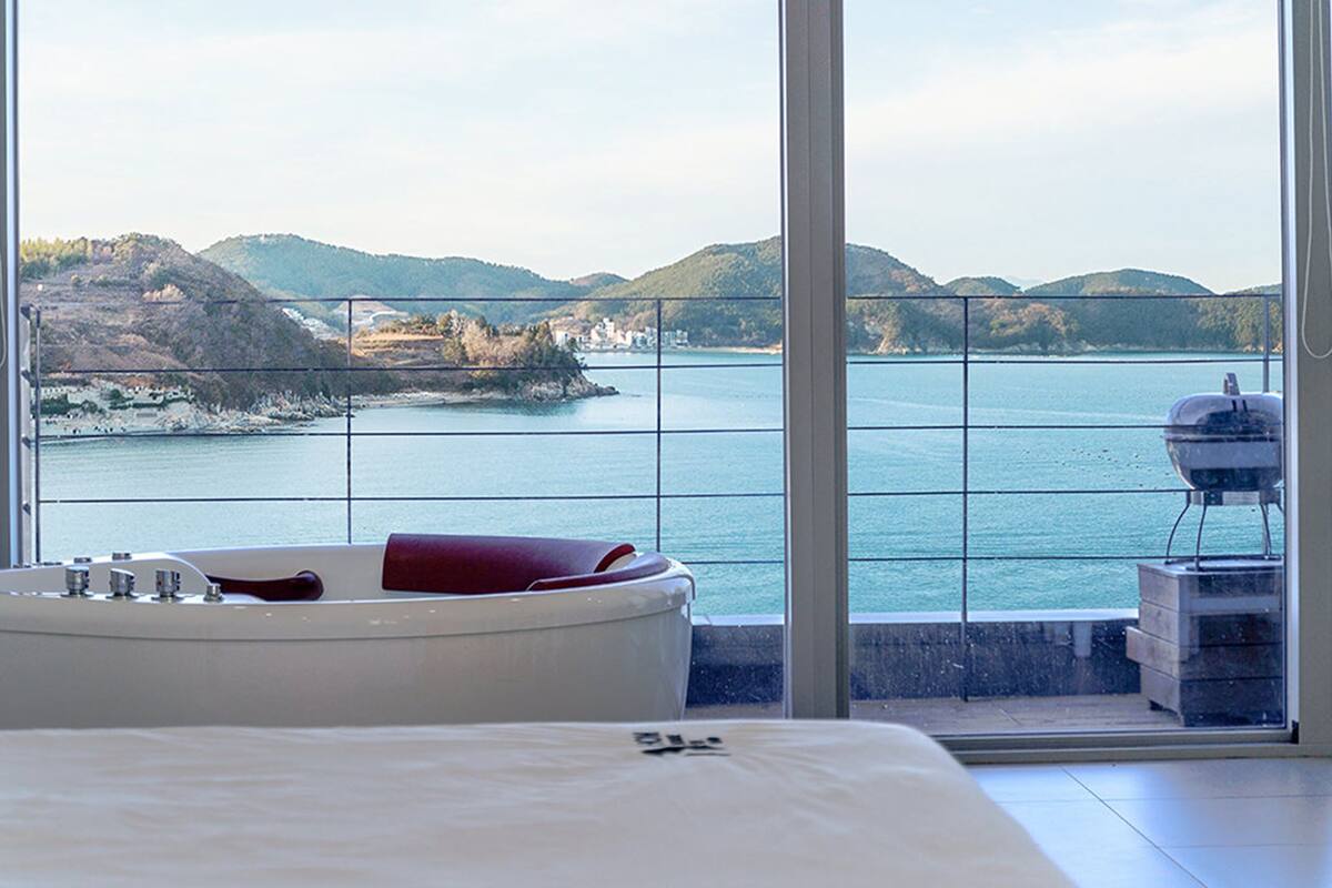 A bedroom with a large window offering a view of a body of water and hills.