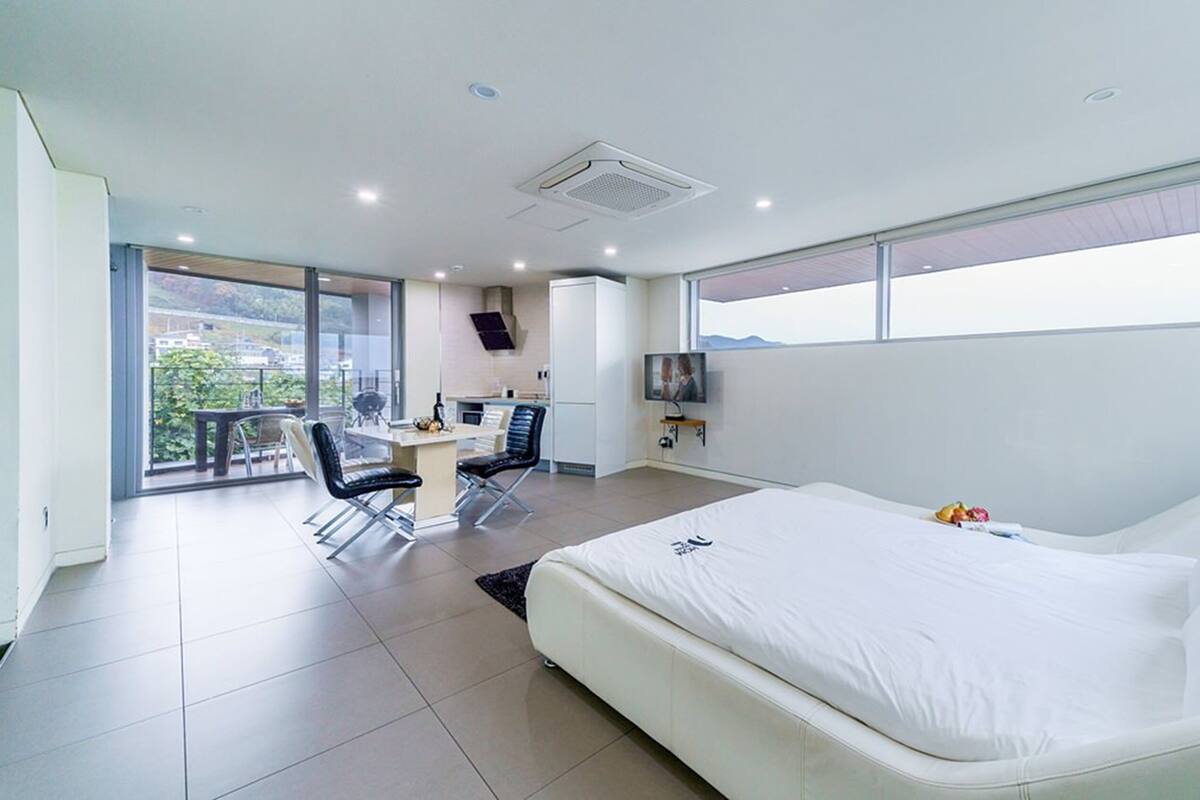 A modern hotel room with a large bed, a desk with a chair, a television, and a balcony with a view.
