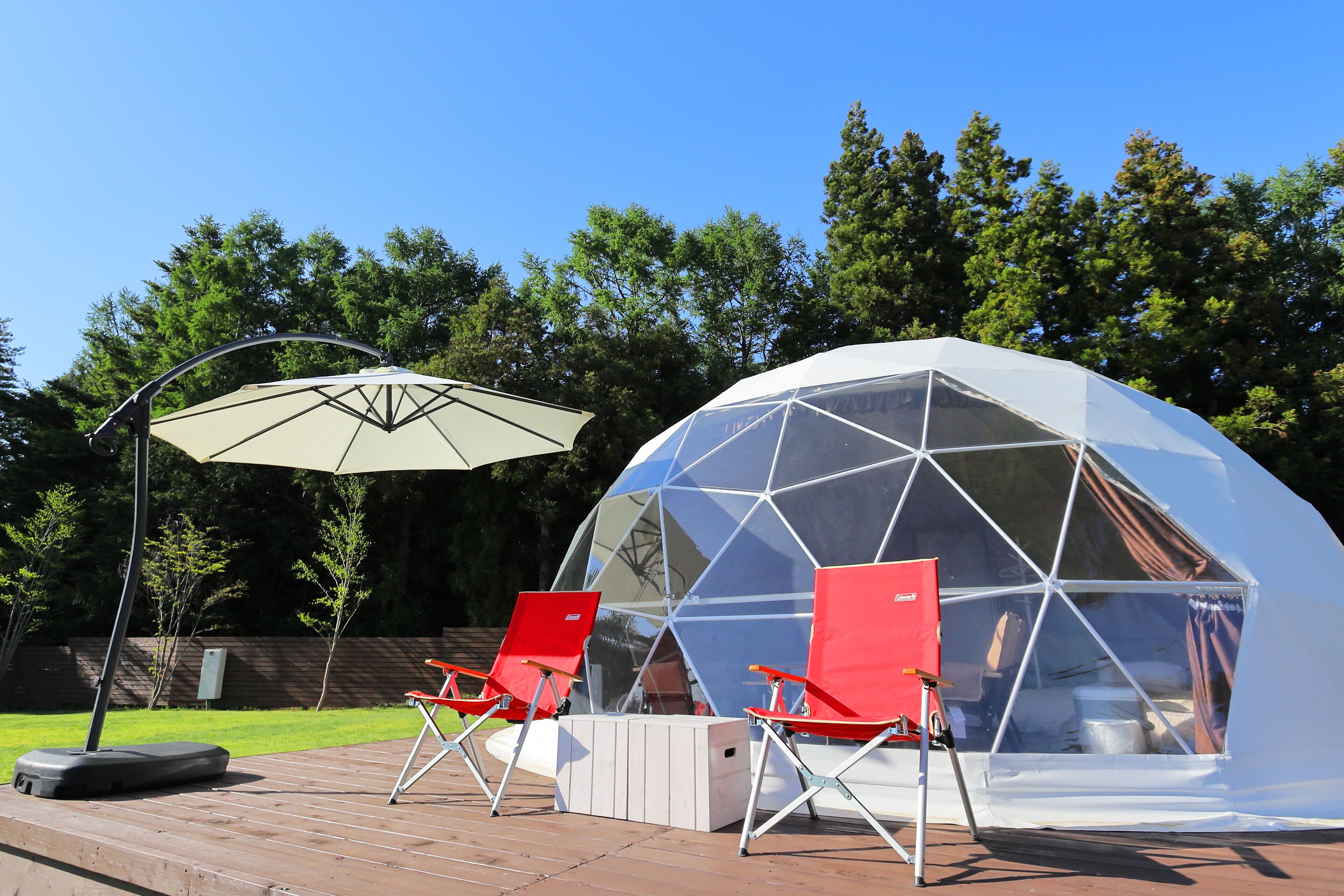 A geodesic dome structure with a transparent roof, surrounded by a wooden deck and red folding chairs.