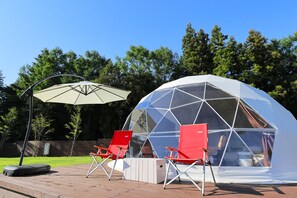 A geodesic dome structure with a transparent roof, surrounded by a wooden deck and red folding chairs. - Mt.Shakushi Gateway Camp (Fujiyoshida)