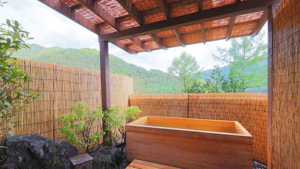 Ein traditionelles japanisches Onsen mit einer hölzernen Thermalbadewanne, Bambuswänden und Blick auf grüne Berge.