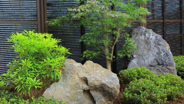A garden with green foliage, a rock formation, and a bamboo fence. - Villas Waraku (Fujiyoshida)