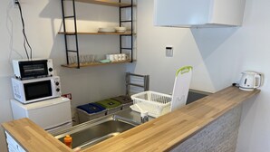 A kitchen with a wooden countertop, a sink, a microwave, a kettle, and a shelf with dishes. - Villas Waraku (Fujiyoshida)