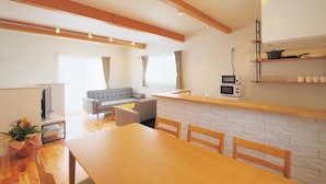 A modern kitchen with a wooden countertop, a built-in microwave, and a small shelf with kitchenware. - Villas Waraku (Fujiyoshida)