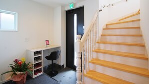 A staircase with wooden steps and white balusters, leading to a door with a green exit sign. - Villas Waraku (Fujiyoshida)