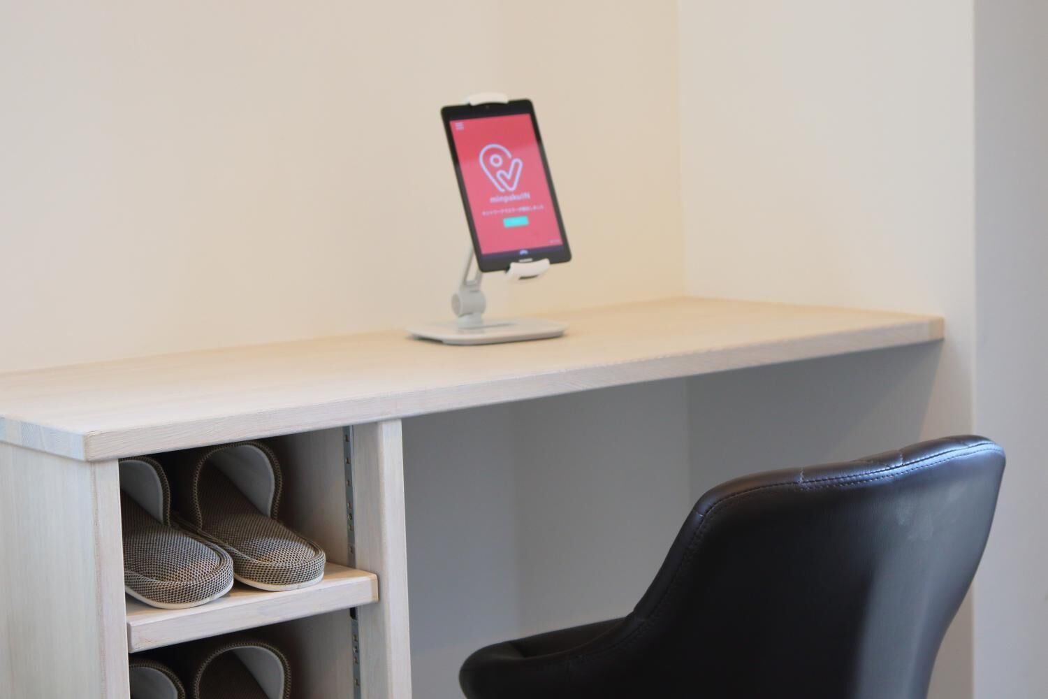 A smartphone on a stand displaying a heart icon, a black chair, and a shelf with shoes.