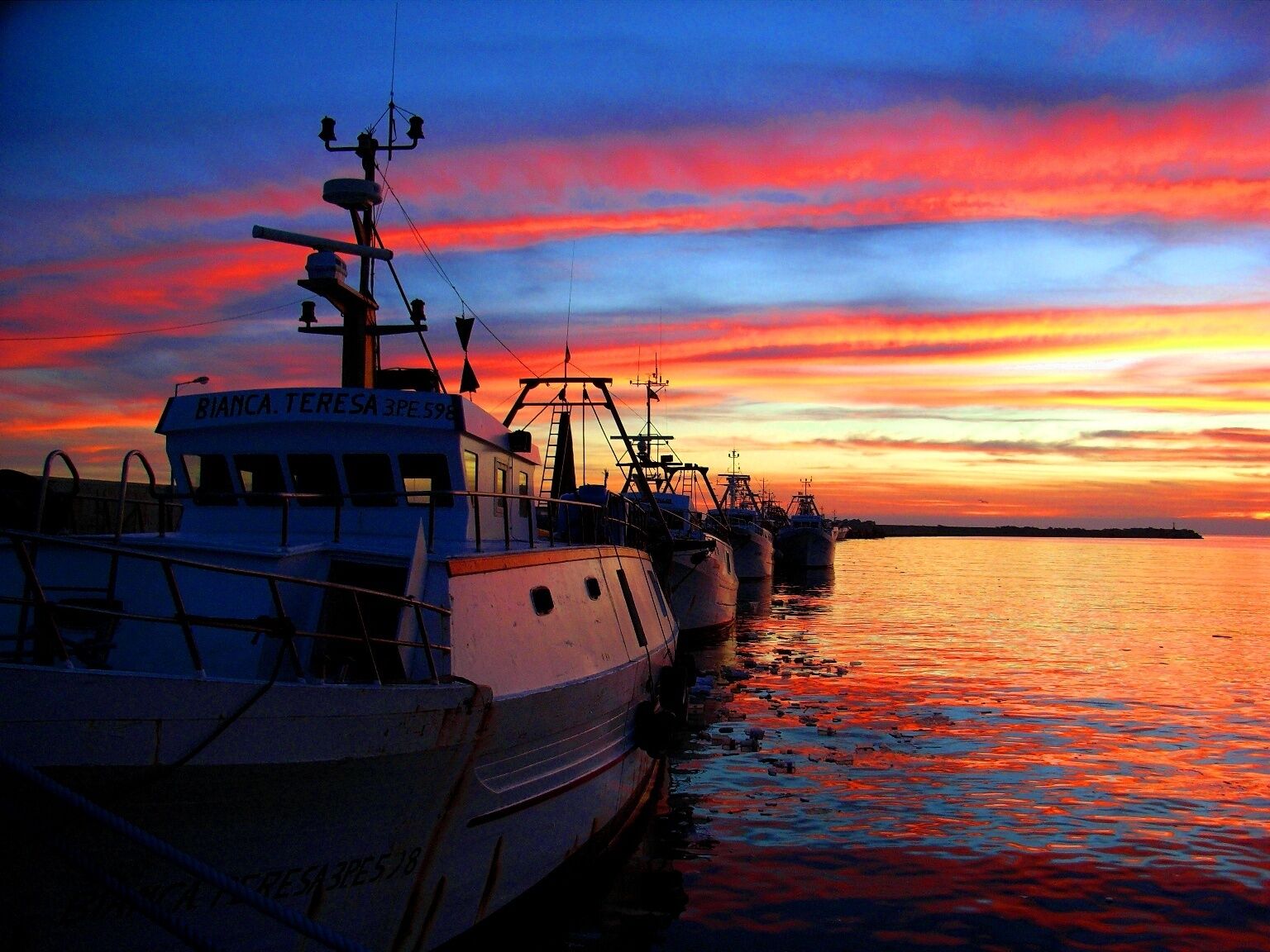 Eine Reihe von Booten liegt im Hafen bei Sonnenuntergang.