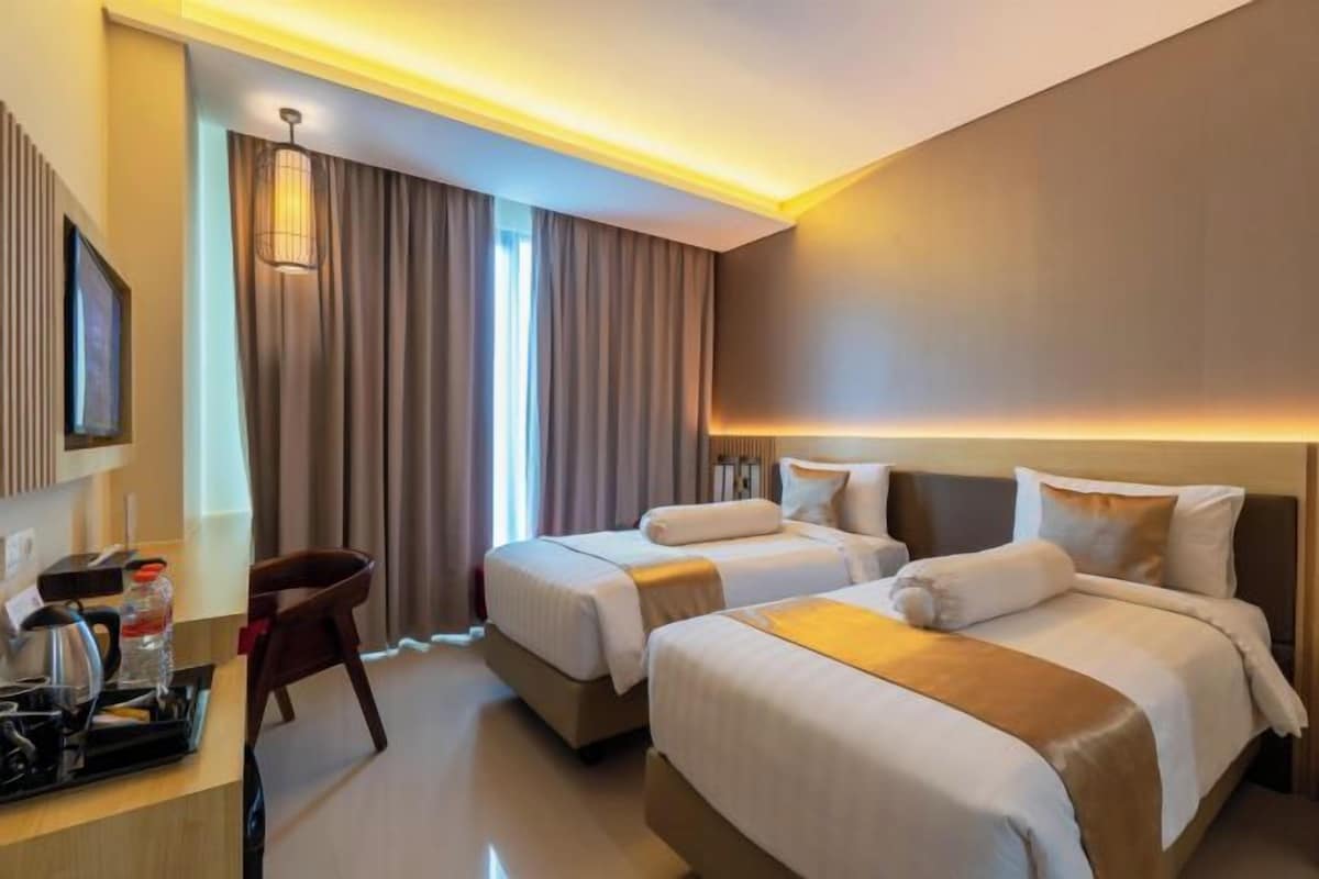 A hotel room with two beds, a desk with a kettle, and a chair.