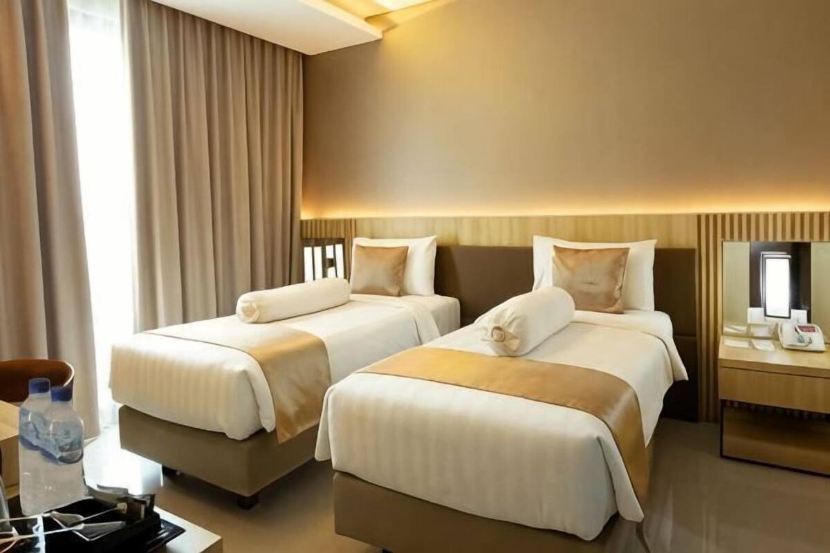 A hotel room with two beds, a desk, a chair, a mirror, and a window with curtains.