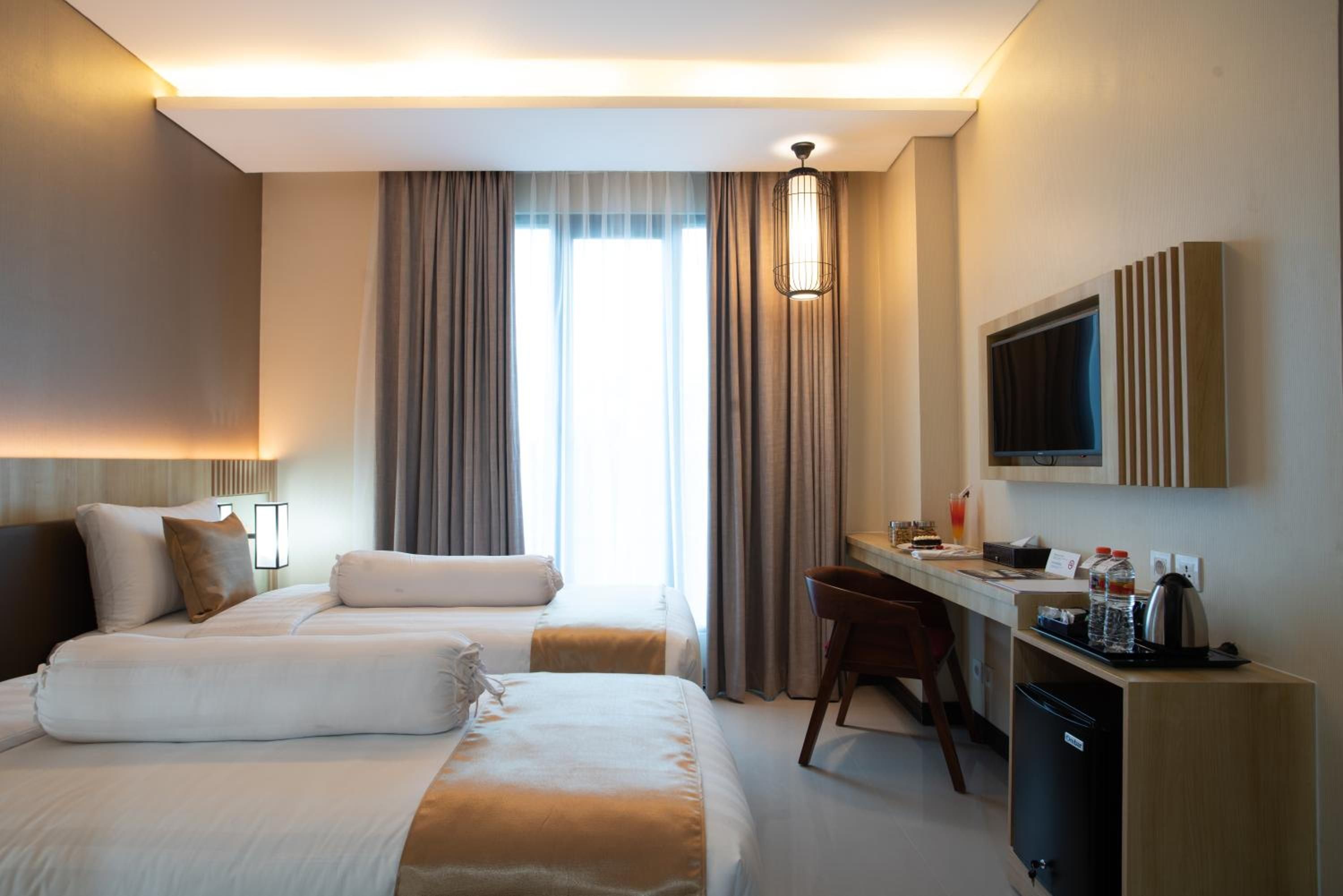 Ein Hotelzimmer mit zwei Betten, einem Schreibtisch, einem Sessel, einem Fernseher und einer Minibar.