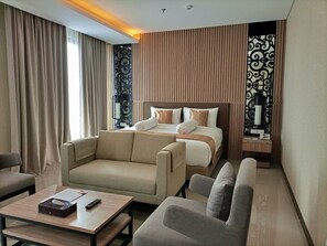 Una habitación de hotel con una cama, dos sofás, una mesa de centro y un escritorio con lámpara.