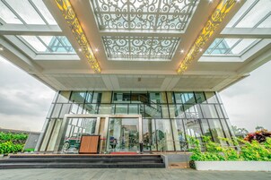 A modern building with a glass facade, a central entrance with a red carpet, and a decorative ceiling design.