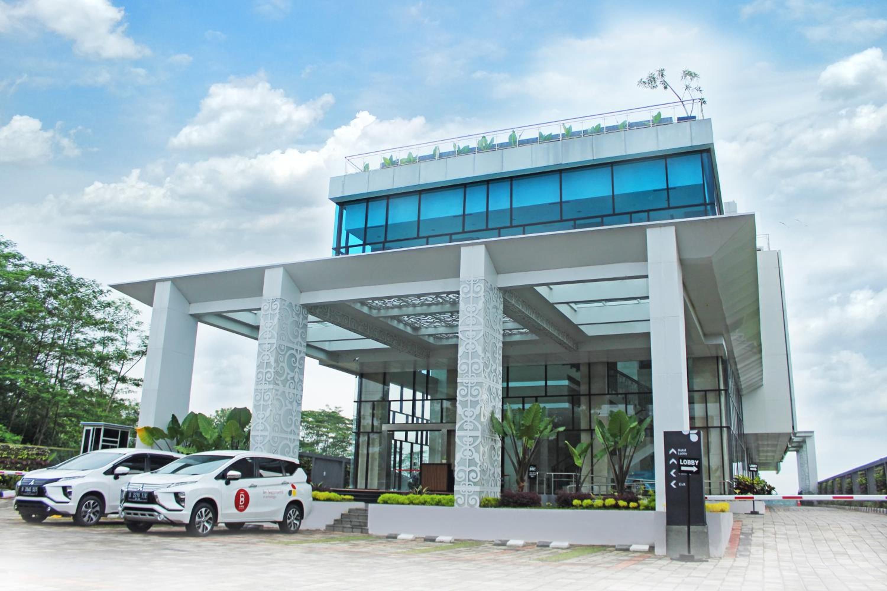 A modern hotel with a glass facade, white columns, and a covered entrance.