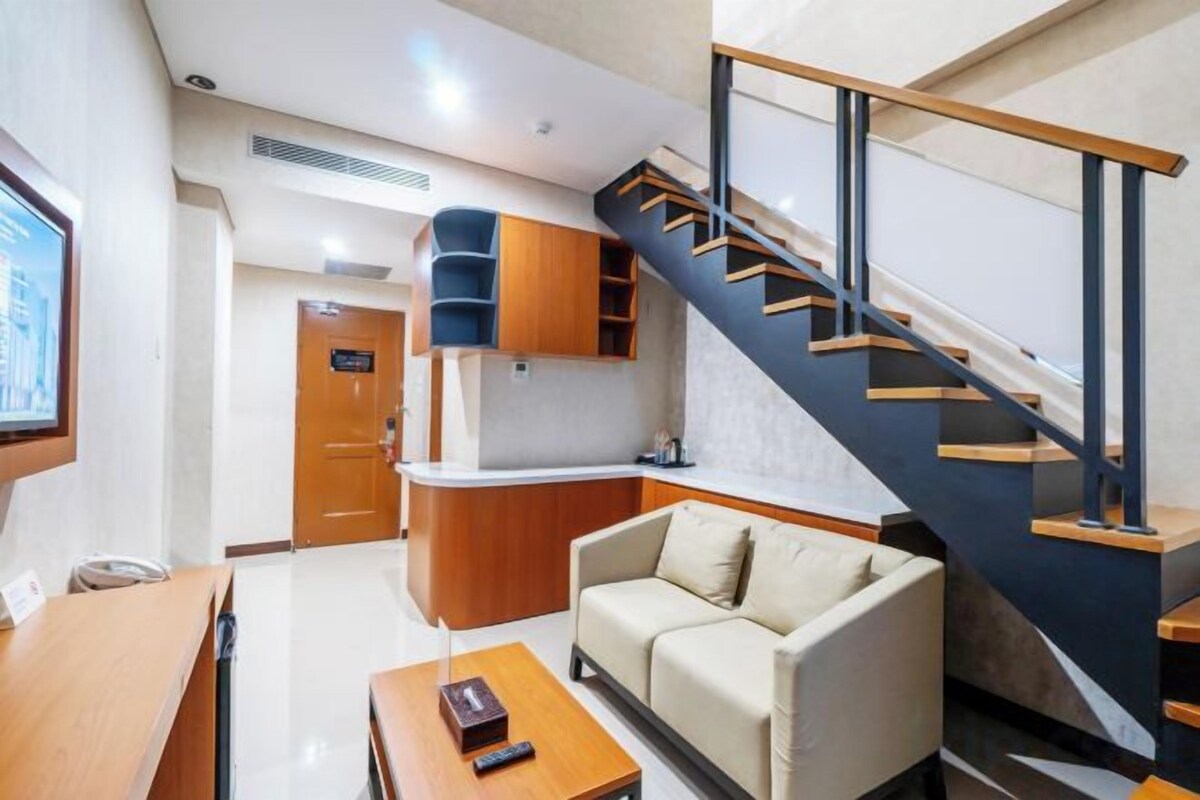Habitación de hotel moderna con sofá, una mesa de centro de madera, televisión y una escalera.