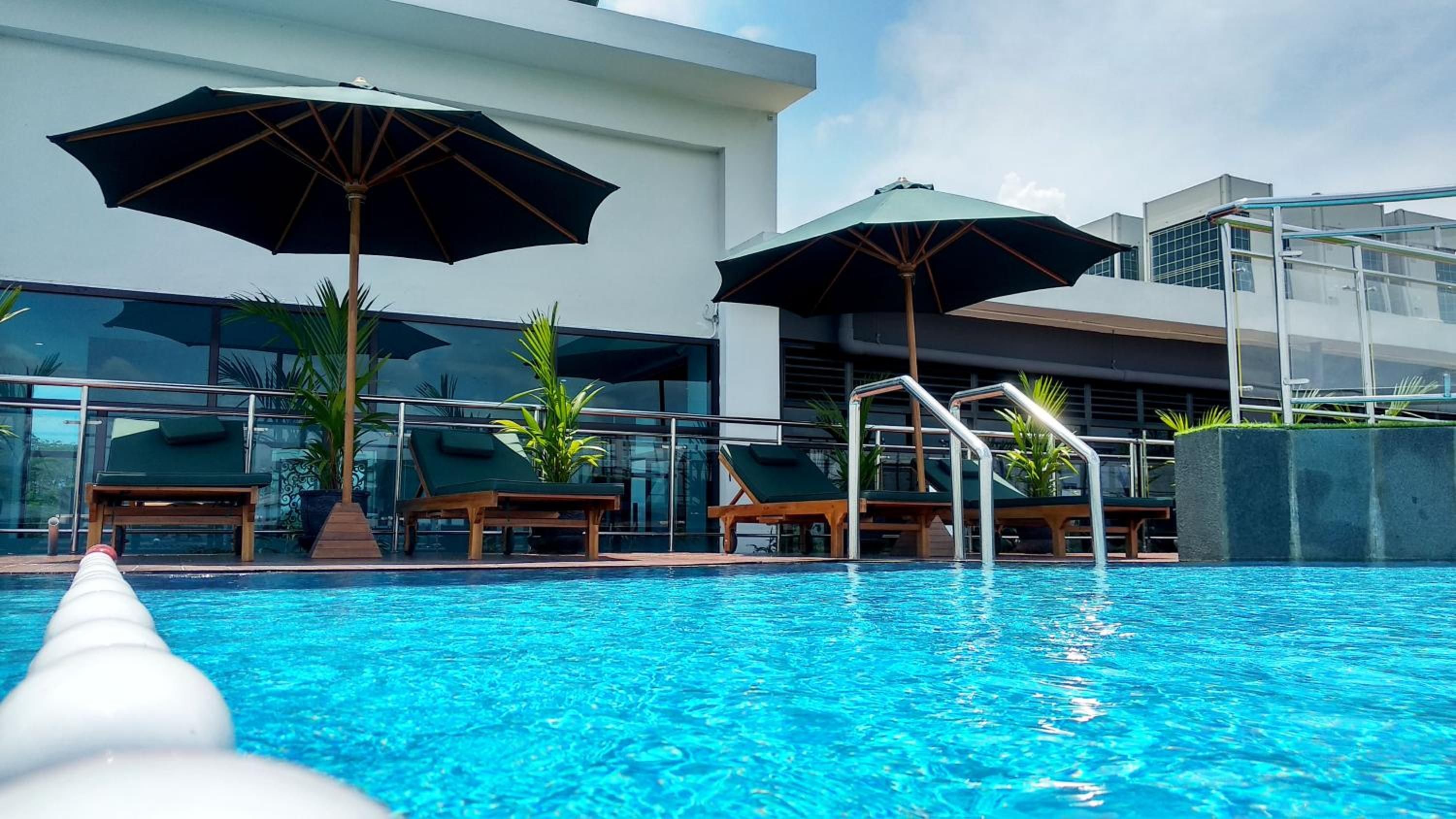 Una piscina con sillones de descanso y sombrillas, rodeada de edificios modernos.