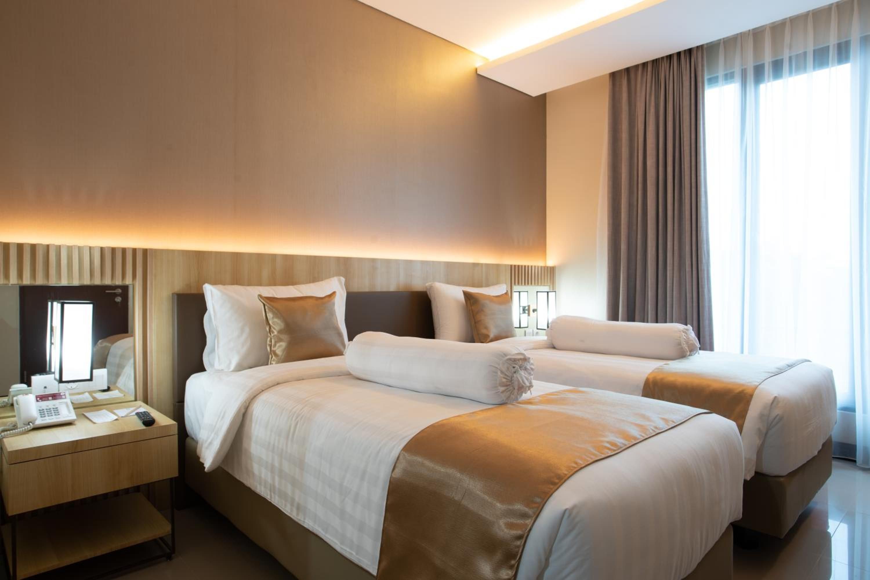 Habitación de hotel con dos camas, un escritorio con teléfono y un ventanal con cortinas.