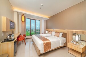 A hotel room with a large bed, a desk with a computer, a TV, and a view of the city.
