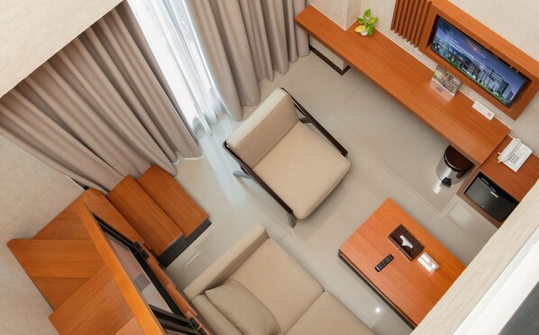 Habitación de hotel con sofá, escritorio, televisor y una mesita con control remoto.