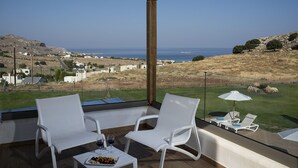 Ein Balkon mit weißen Stühlen und einem Tisch, der auf eine Küstenlandschaft mit Häusern und dem Meer blickt.