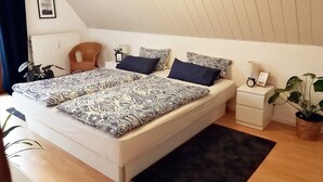 Un dormitorio con cama, una silla, una mesita de noche, una lámpara, un reloj y una planta en maceta.