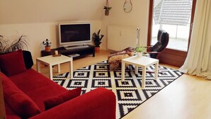 Una sala de estar con un sofá rojo, un televisor, una mesita blanca pequeña y una alfombra estampada.