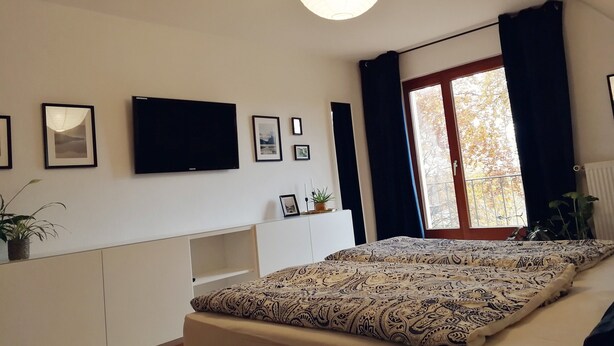 Un dormitorio con cama, televisión, ventana con cortinas e imágenes colgadas en la pared.