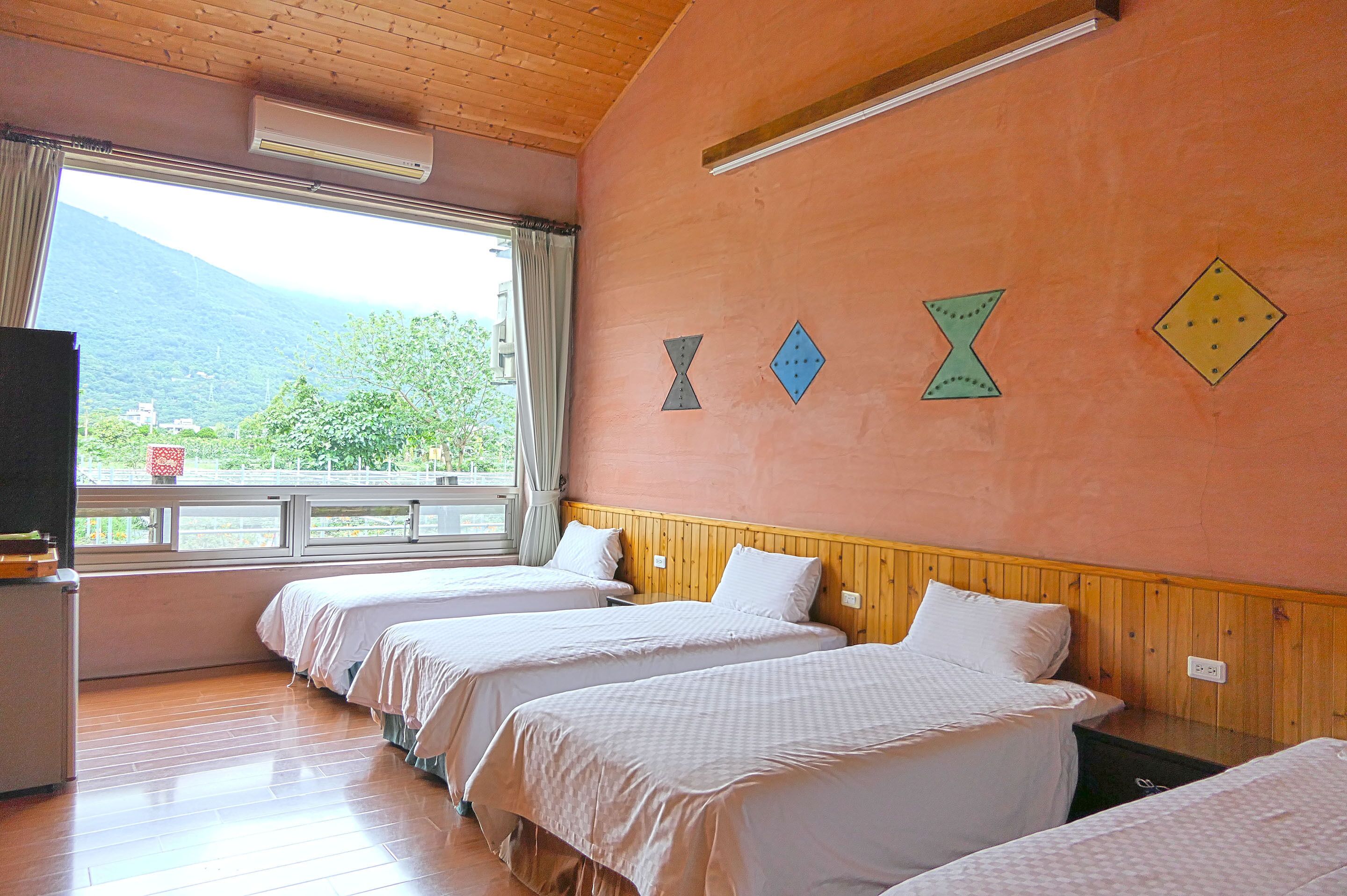 A hotel room with three beds, wooden paneling, a large window with a view of mountains, and decorative wall art.