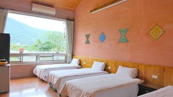 A hotel room with three beds, wooden paneling, a large window with a view of mountains, and decorative wall art.